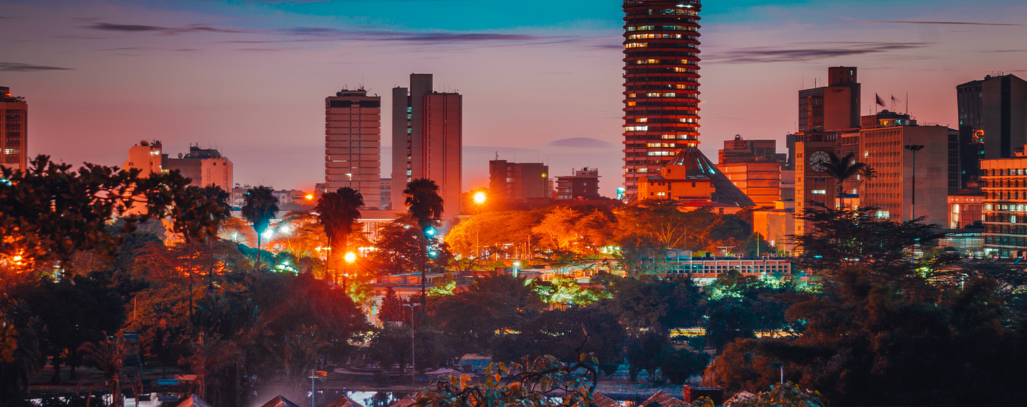 Nairobi's skyline glows at dusk, with illuminated high-rises rising above a foreground of dense city trees