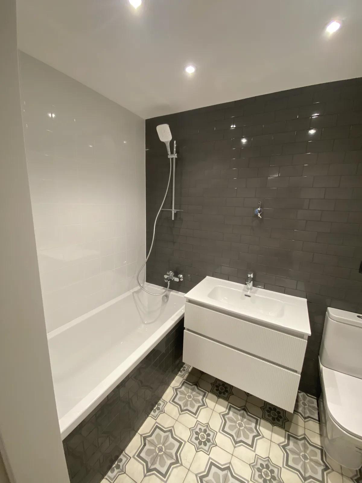 Baño reformado con azulejo tipo metro gris, suelo hidráulico y mueble de lavabo blanco