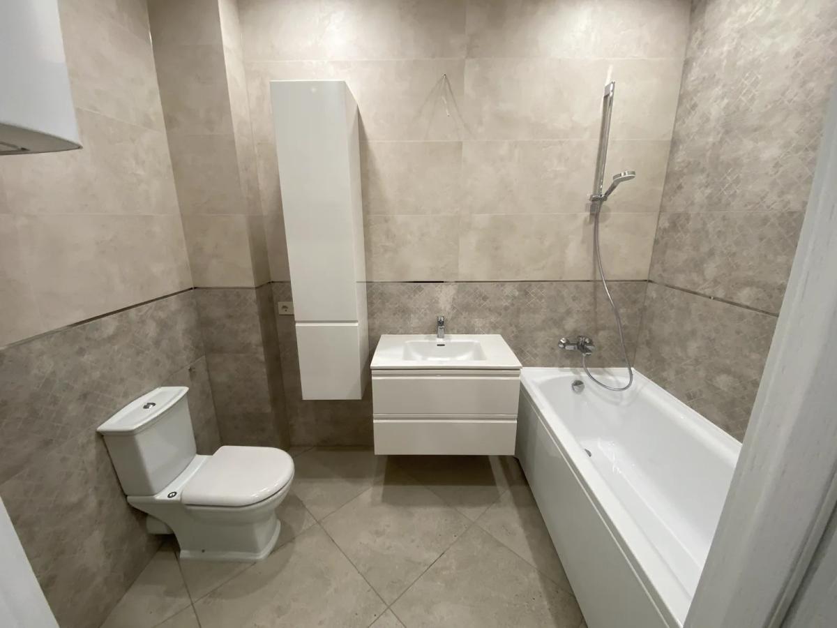 Reforma de baño en Valencia con azulejo beige, mueble suspendido blanco, columna y bañera