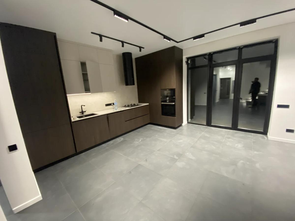 Cocina abierta con muebles en madera oscura, iluminación en carril y salida a la terraza