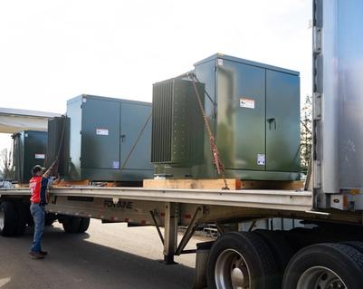 Green padmounted transformers being loaded onto a flatbed truck for shipping