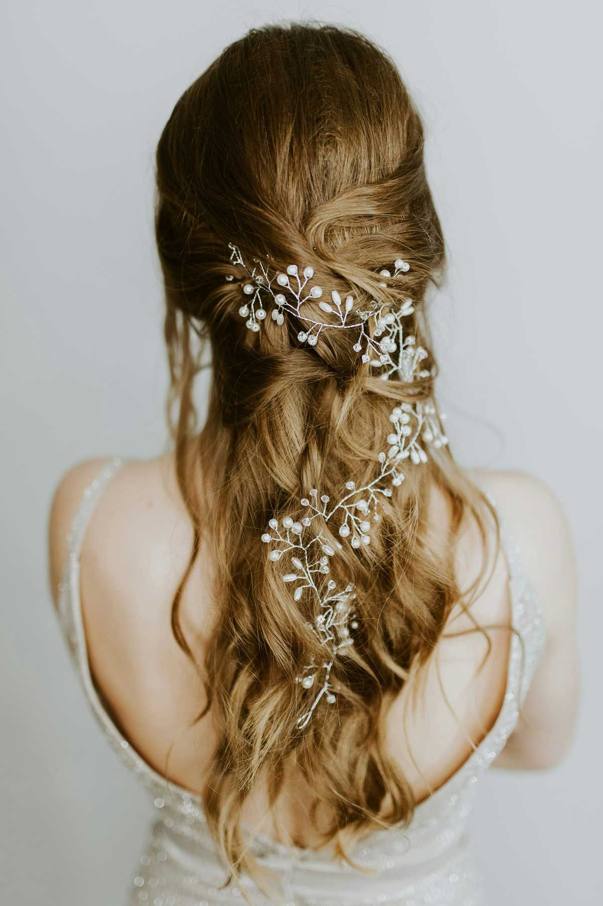 The back of a long, loosely waved half-up hairstyle threaded with a pearl hair vine