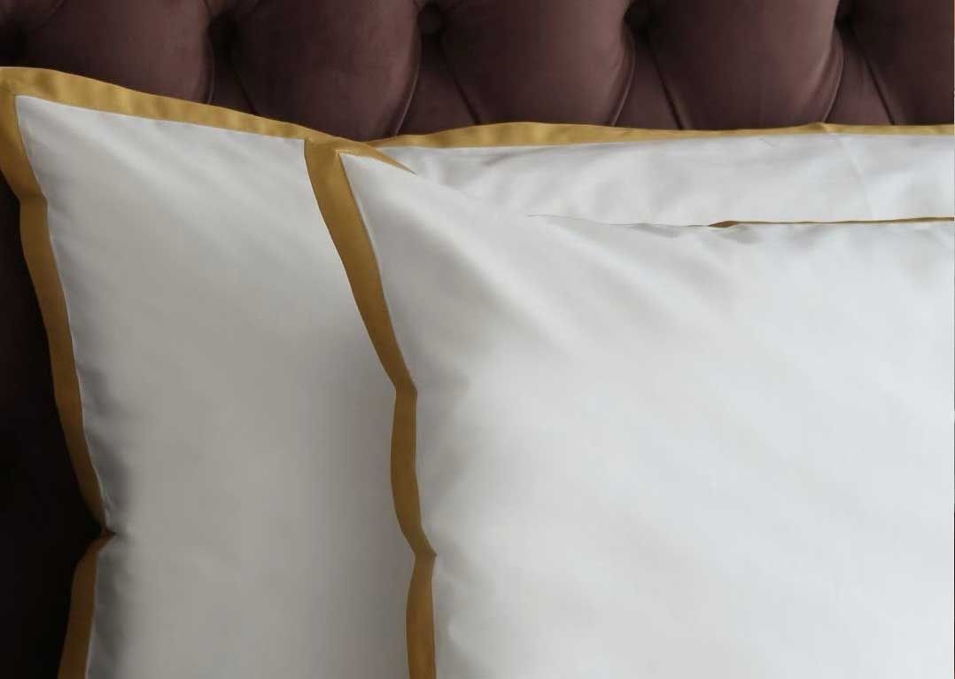 White pillowcases edged in gold against a deep-buttoned plum velvet headboard.