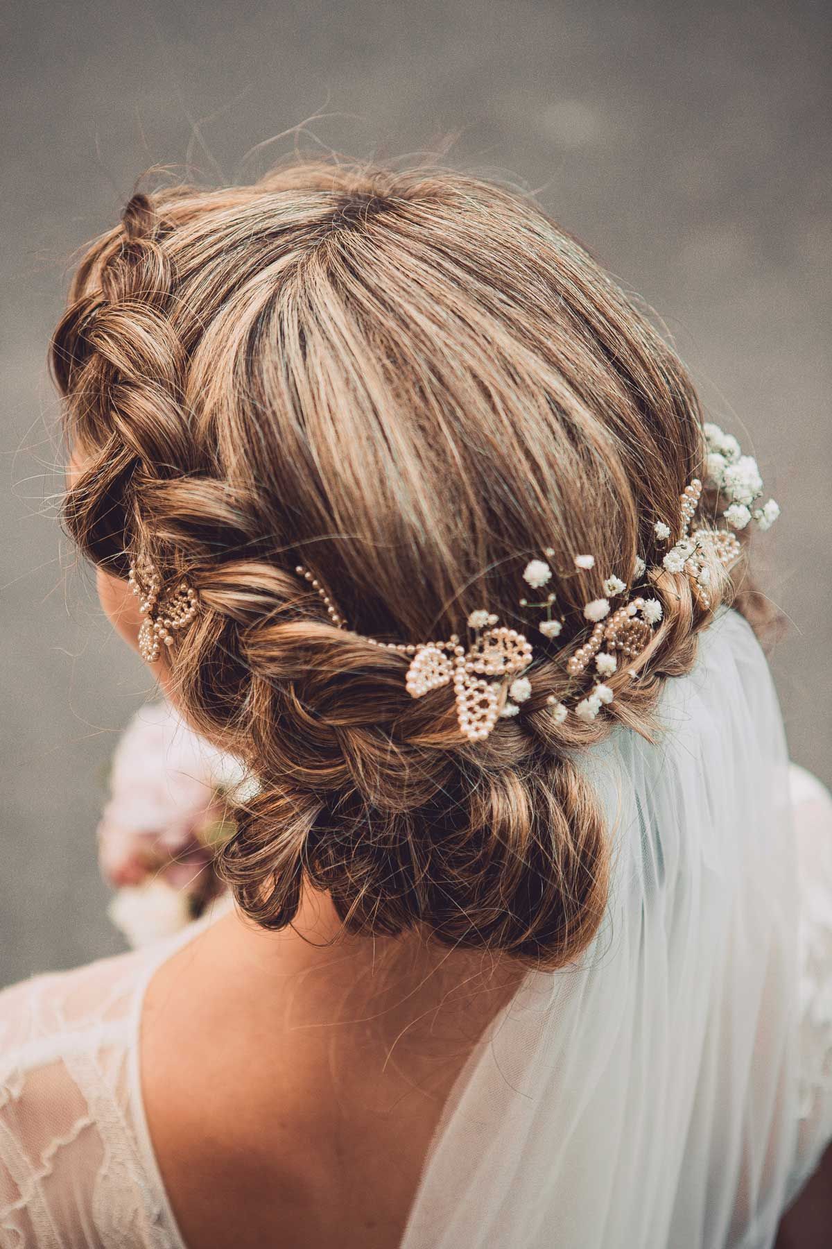A braided updo decorated with pearl and flower pins, worn with a veil