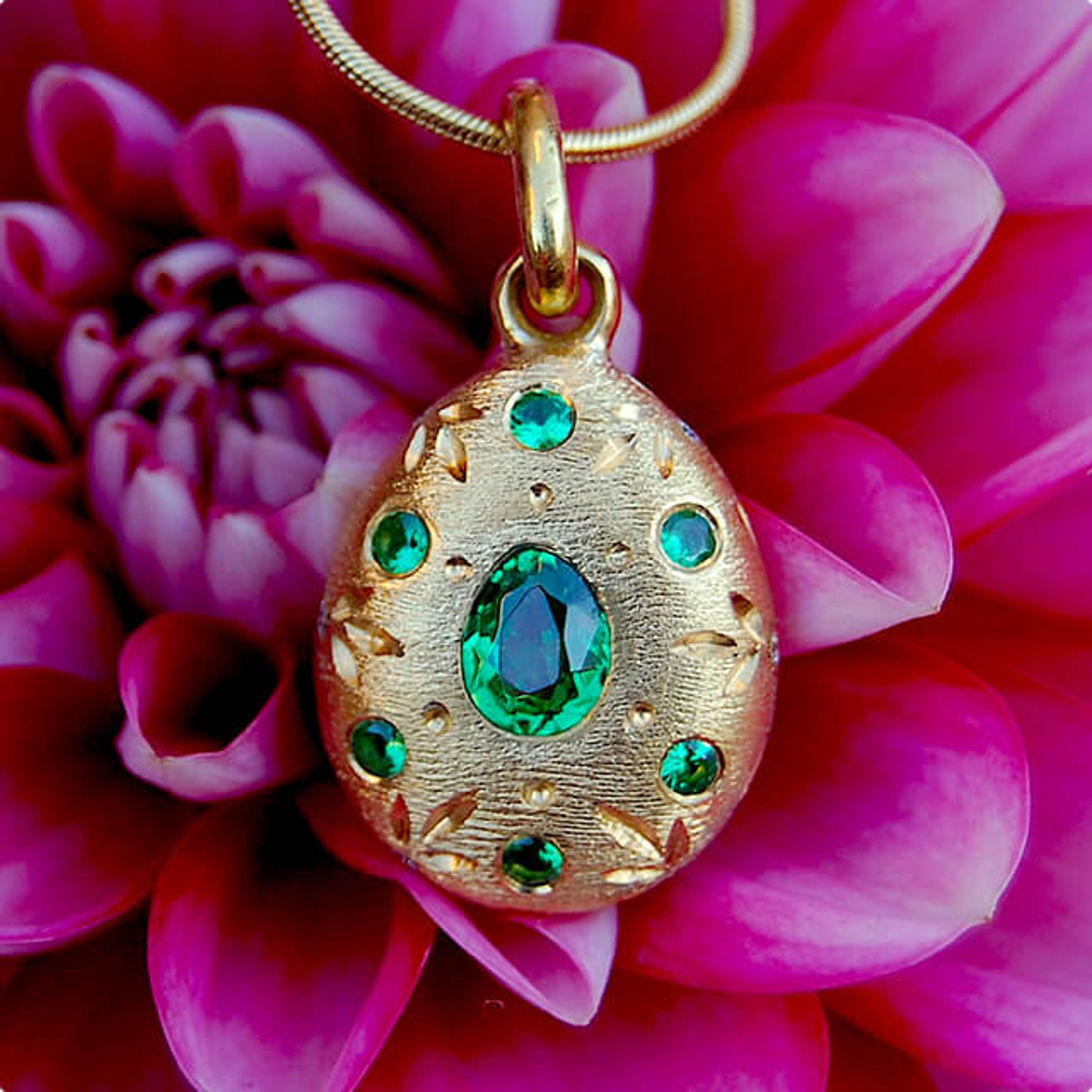 Gold pendant engraved with leaf designs and green gems