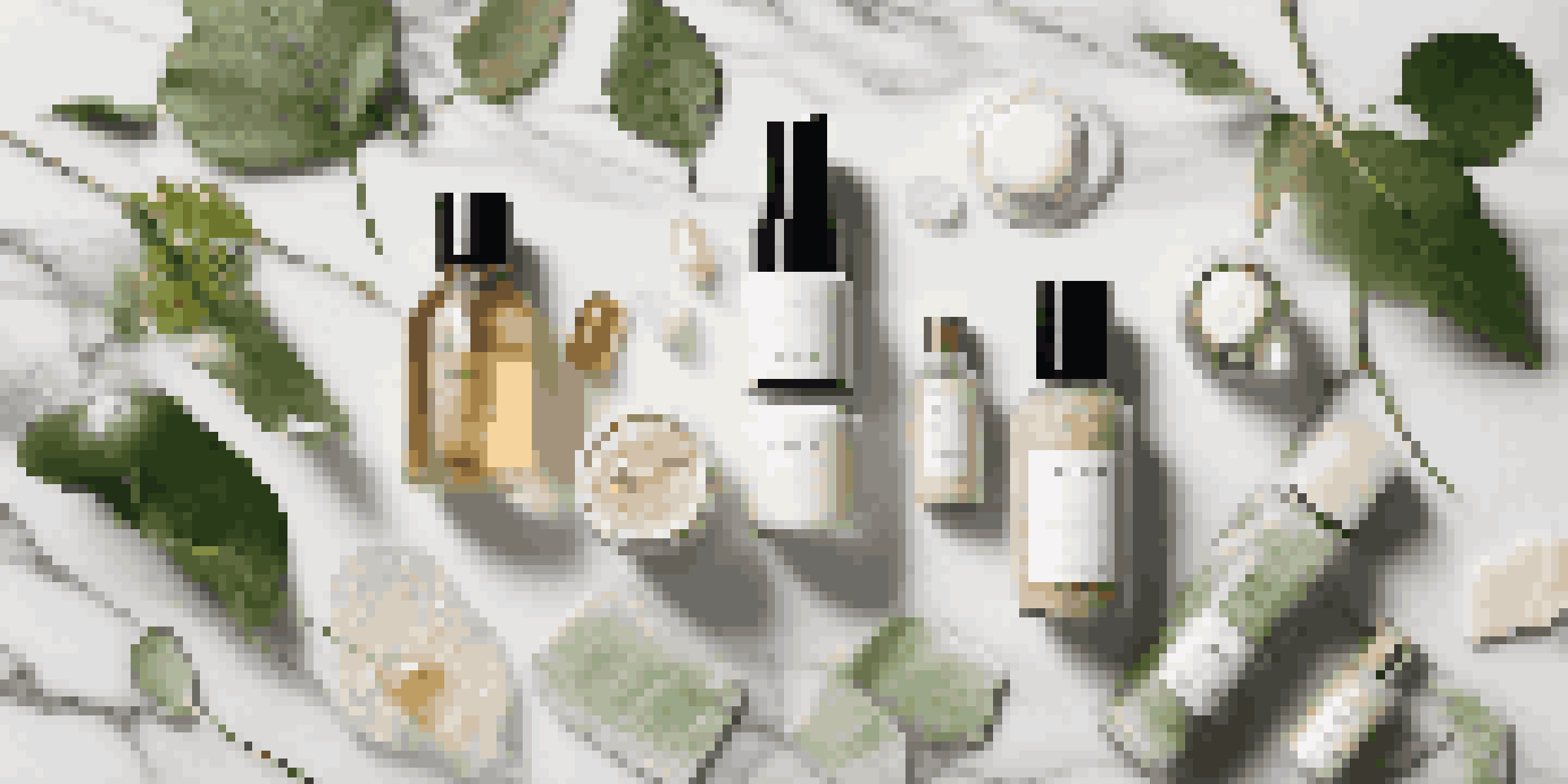 A flat lay of luxury clean beauty products on a marble surface with soft natural lighting and green leaves.