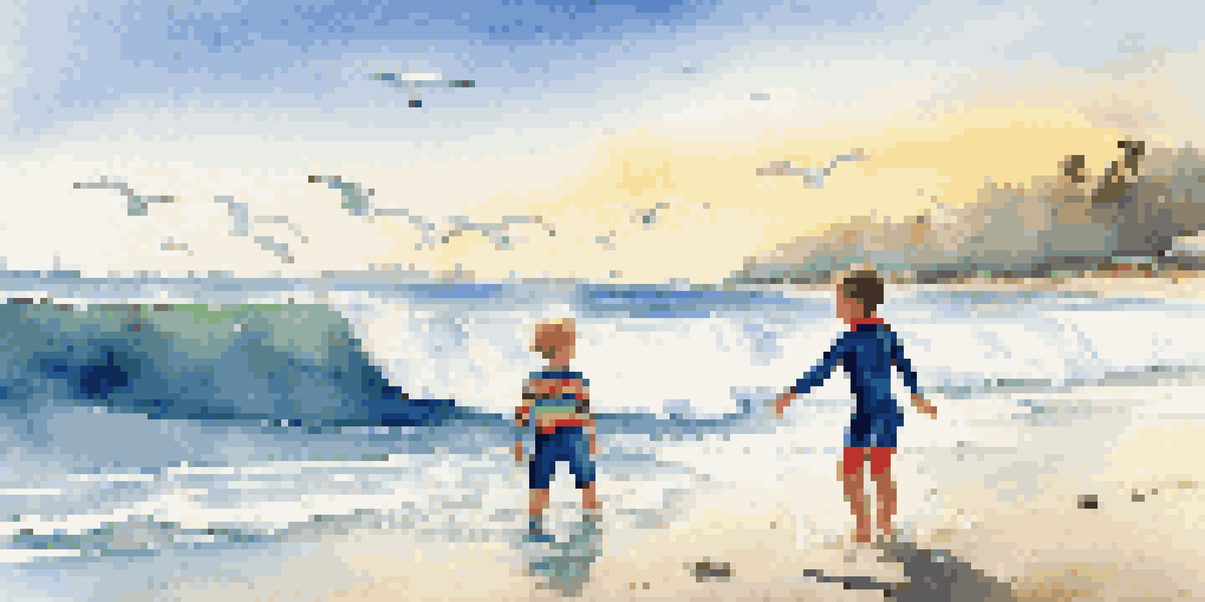 A child wearing a colorful wetsuit rides a small wave, with an instructor watching nearby against a backdrop of a clear blue sky and gentle sunlight.