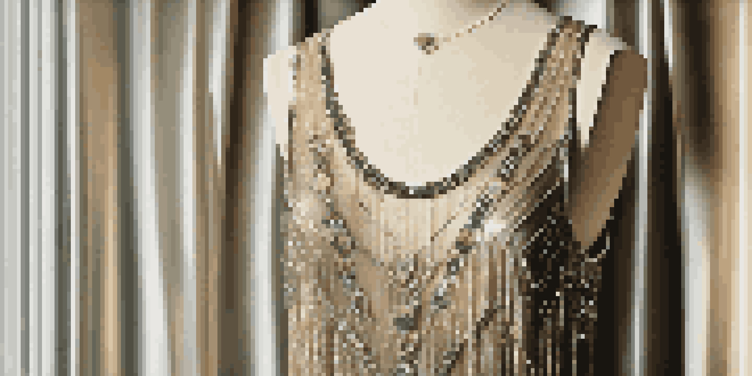 A vintage 1920s flapper dress on a mannequin with beadwork and fringe, blurred background with dim lighting and an antique mirror reflecting the dress.