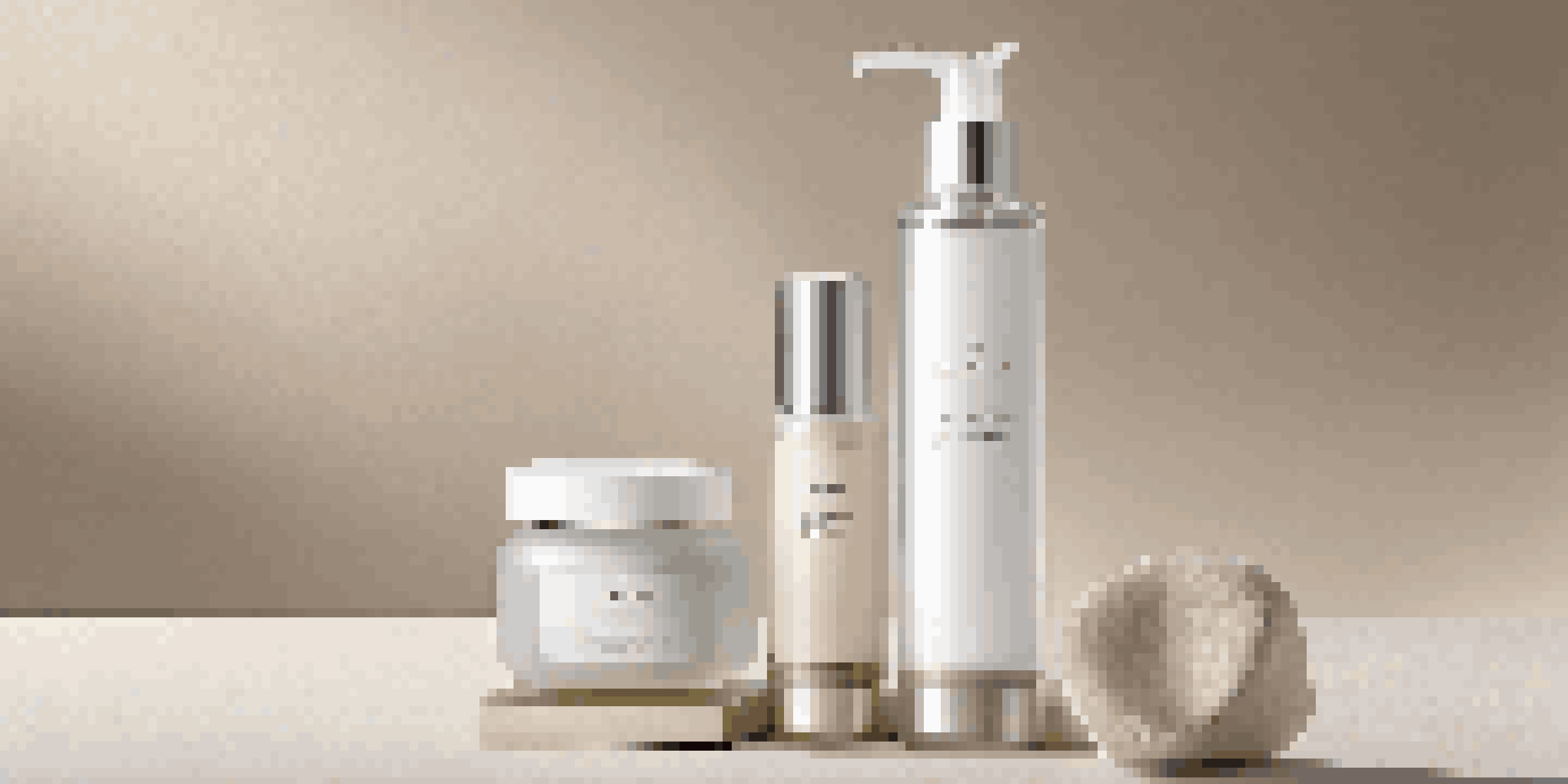 A display of luxurious personal care products in glass and aluminum packaging, arranged on neutral fabric with soft lighting.