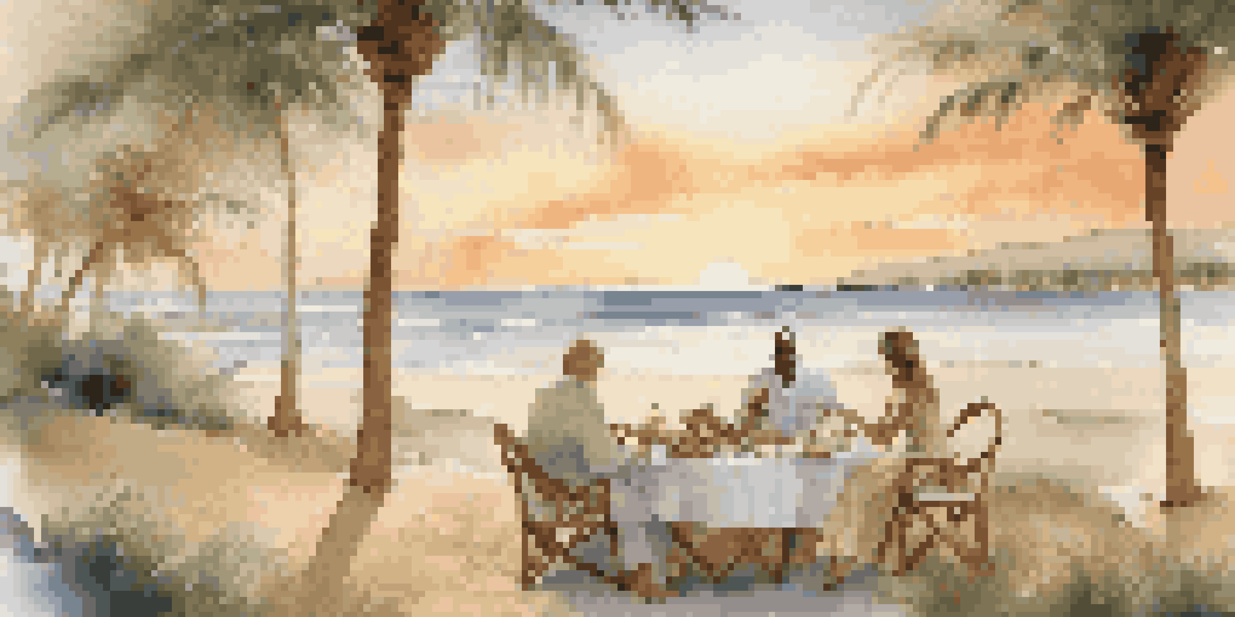 A picturesque beach at sunset with a picnic setup and a couple enjoying their time together amidst palm trees.