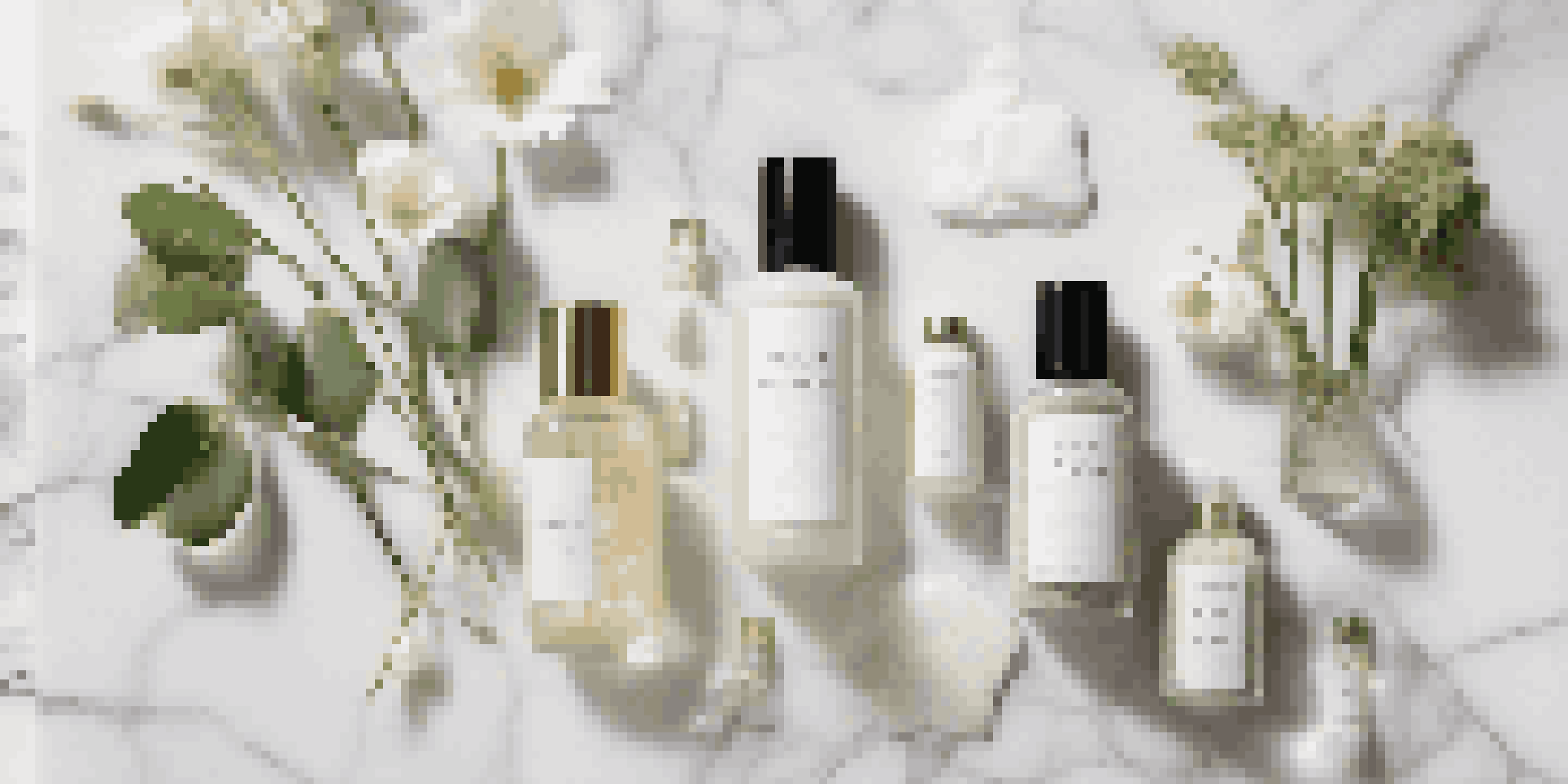 A top view of luxury clean beauty products on a marble surface, with glass containers and natural elements like leaves and a flower.