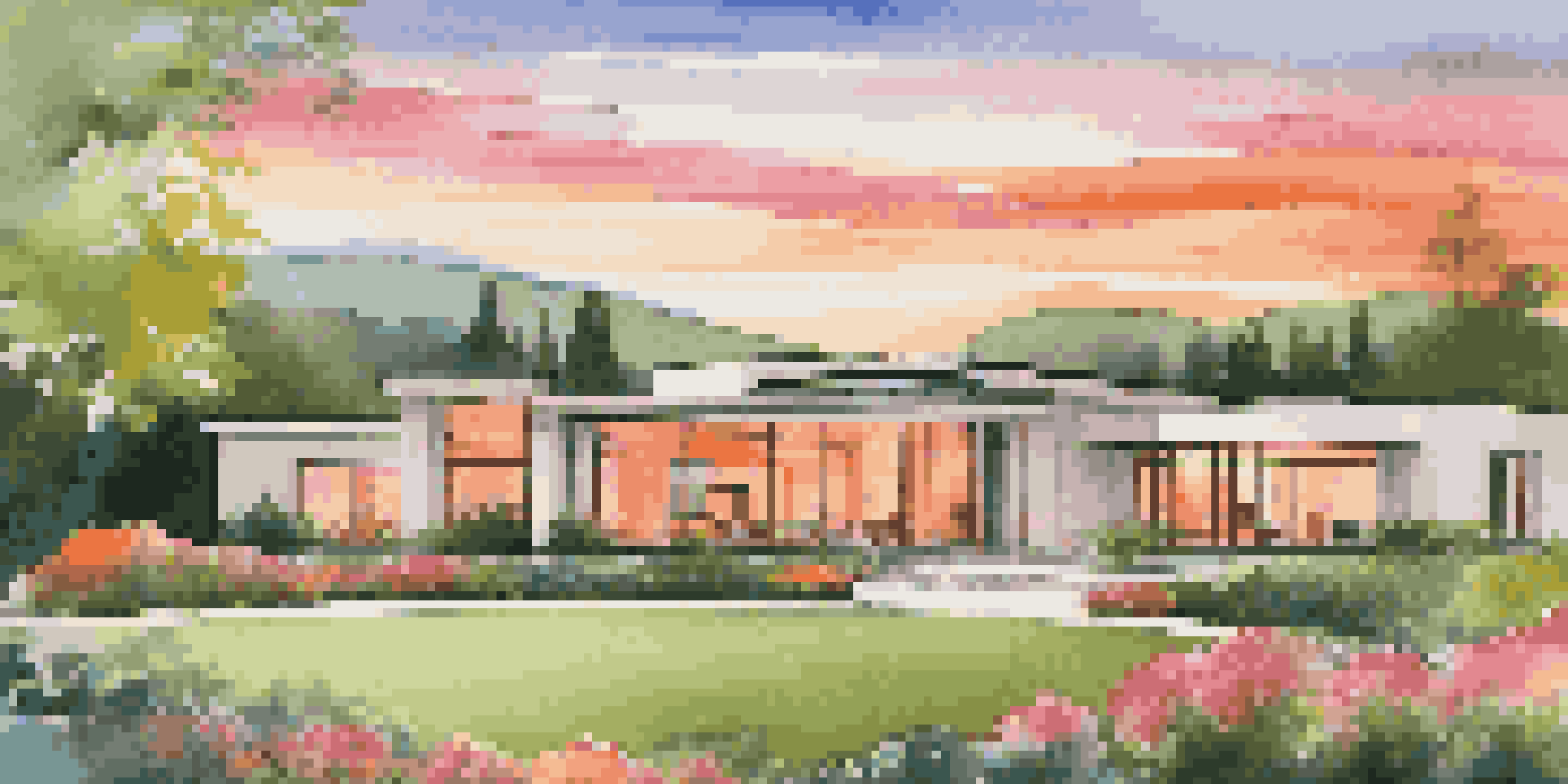 A modern luxury home surrounded by a manicured garden at sunset, with hills in the background.