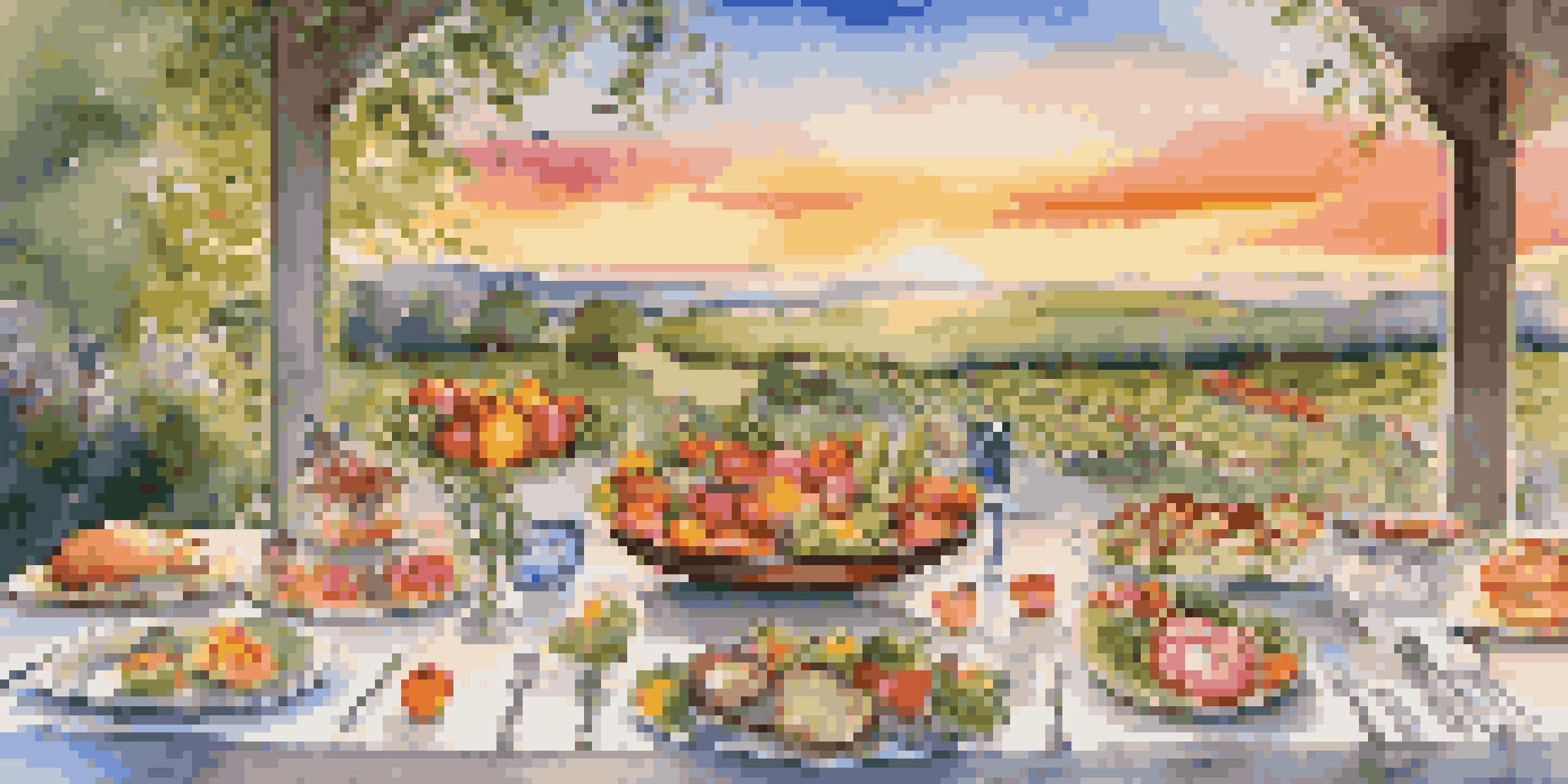 An outdoor gourmet dining table displaying colorful seasonal dishes with elegant tableware and a sunset in the background.