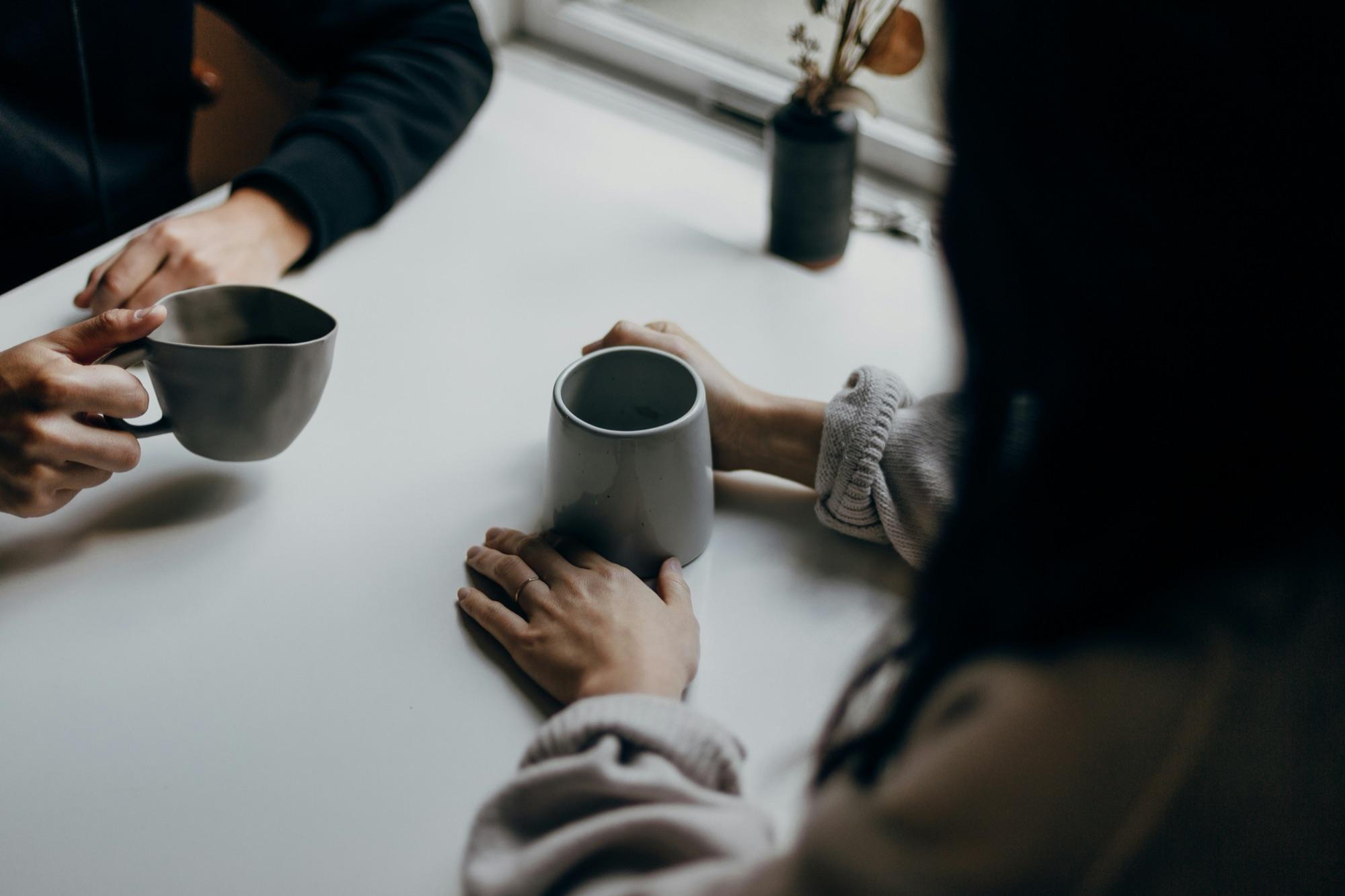 Two people talking across a table with cups of coffee