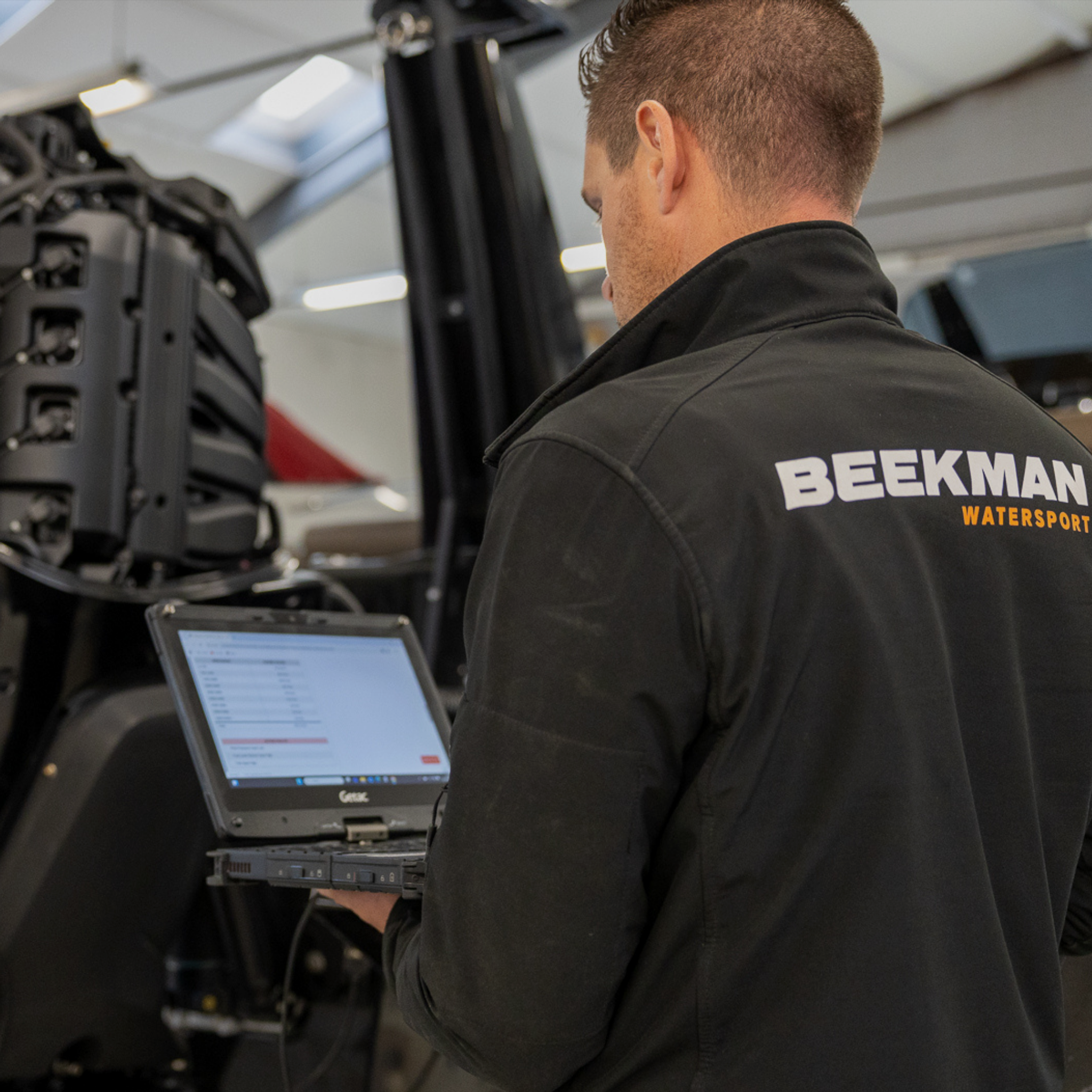 Monteur van Beekman Watersport aan het werk bij een buitenboordmotor, met het logo van Beekman Watersport