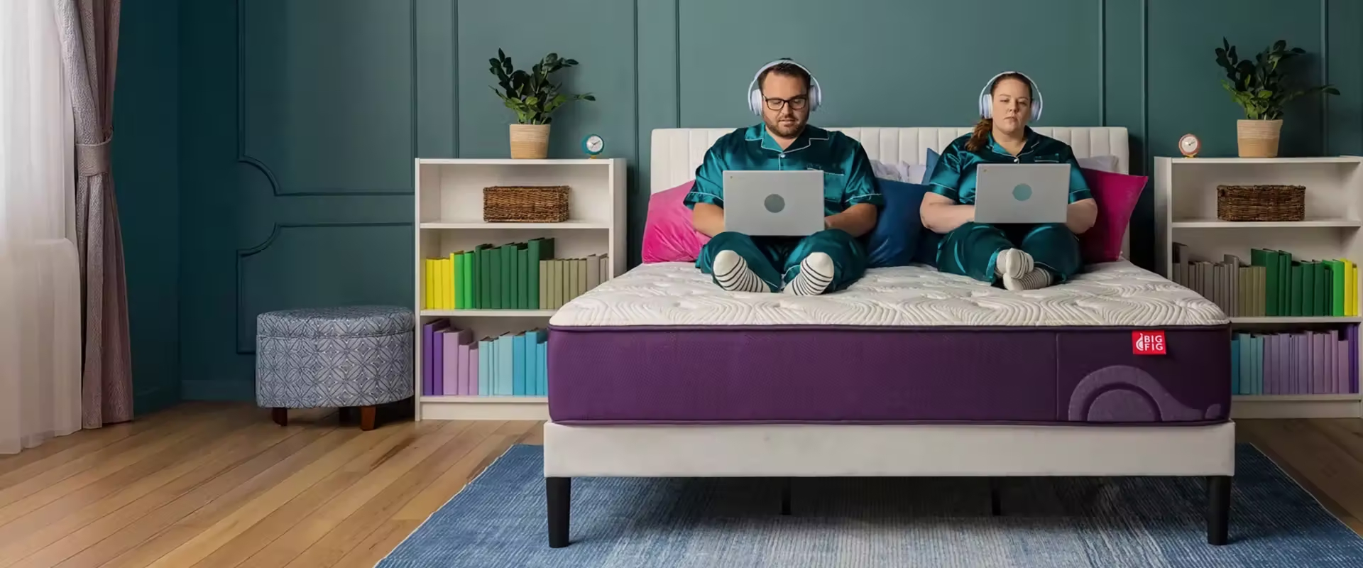 Couple in bed with headphones and laptops with a teal wall and teal pajamas