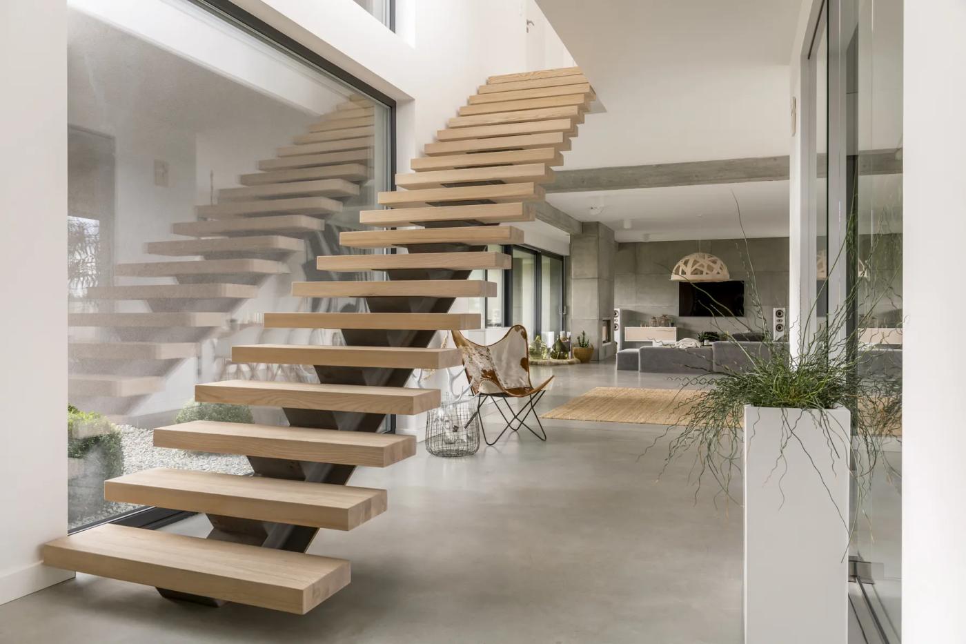 Floating wooden staircase with glass railings in a bright, open-plan home.