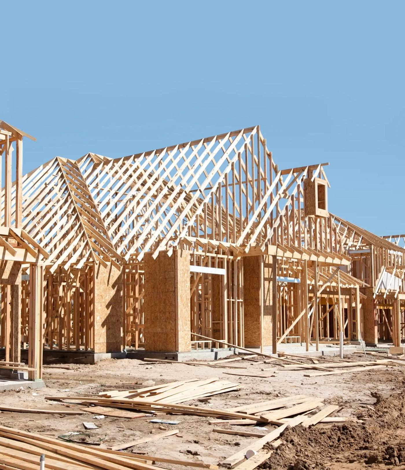 Timber framing and roof trusses of a house under construction beneath a clear blue sky.