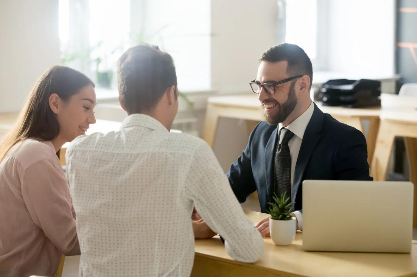 Two people meeting with a suited advisor at a desk with a laptop.
