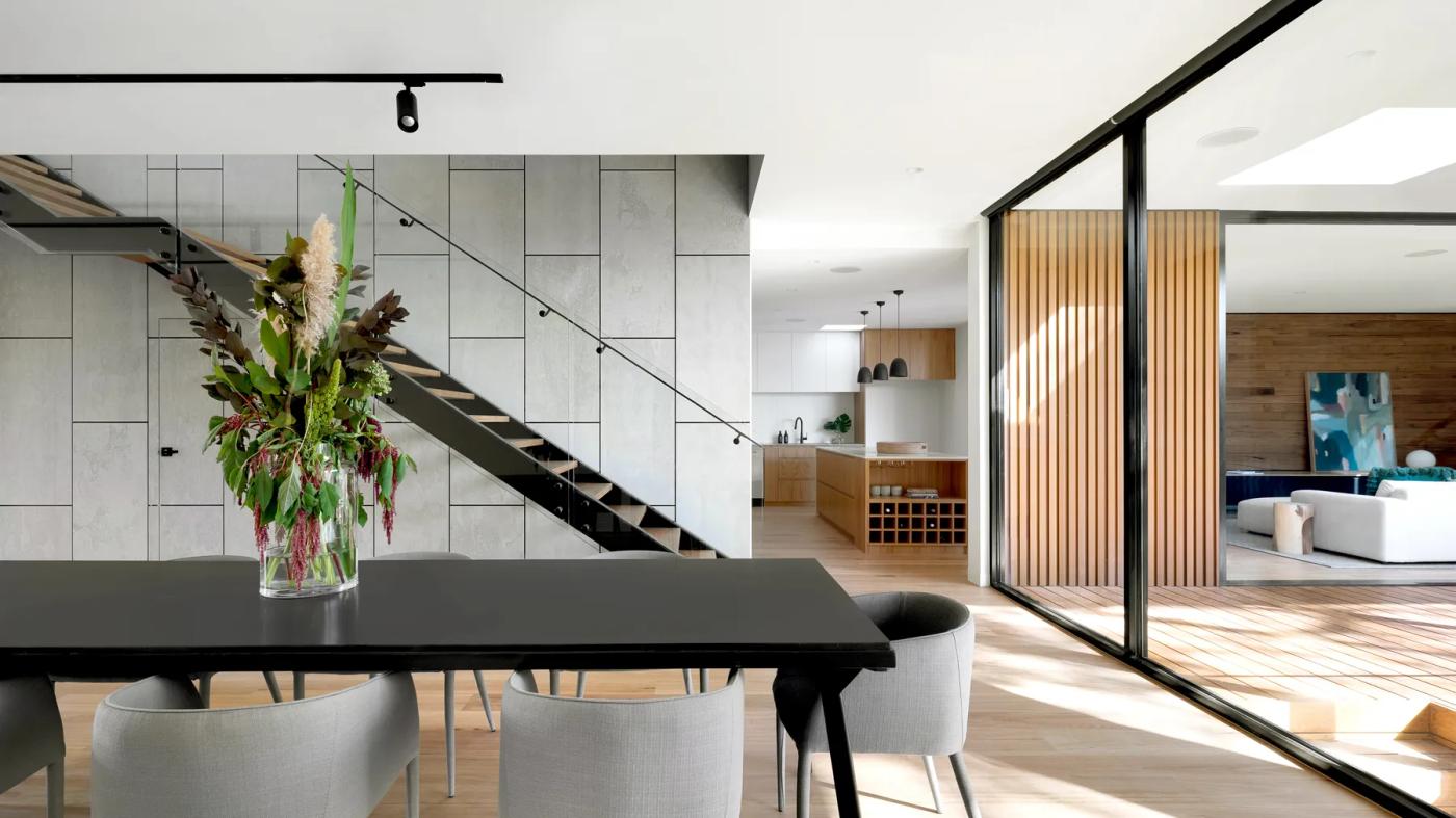 Modern dining area with a black table, open staircase, and sliding glass doors to an adjoining living space.