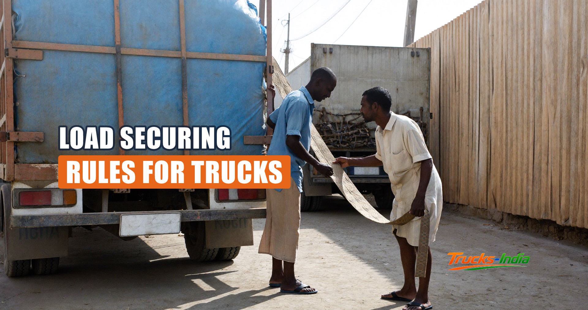 Two loaders pulling a webbing strap over the load on an open body truck in an Indian yard