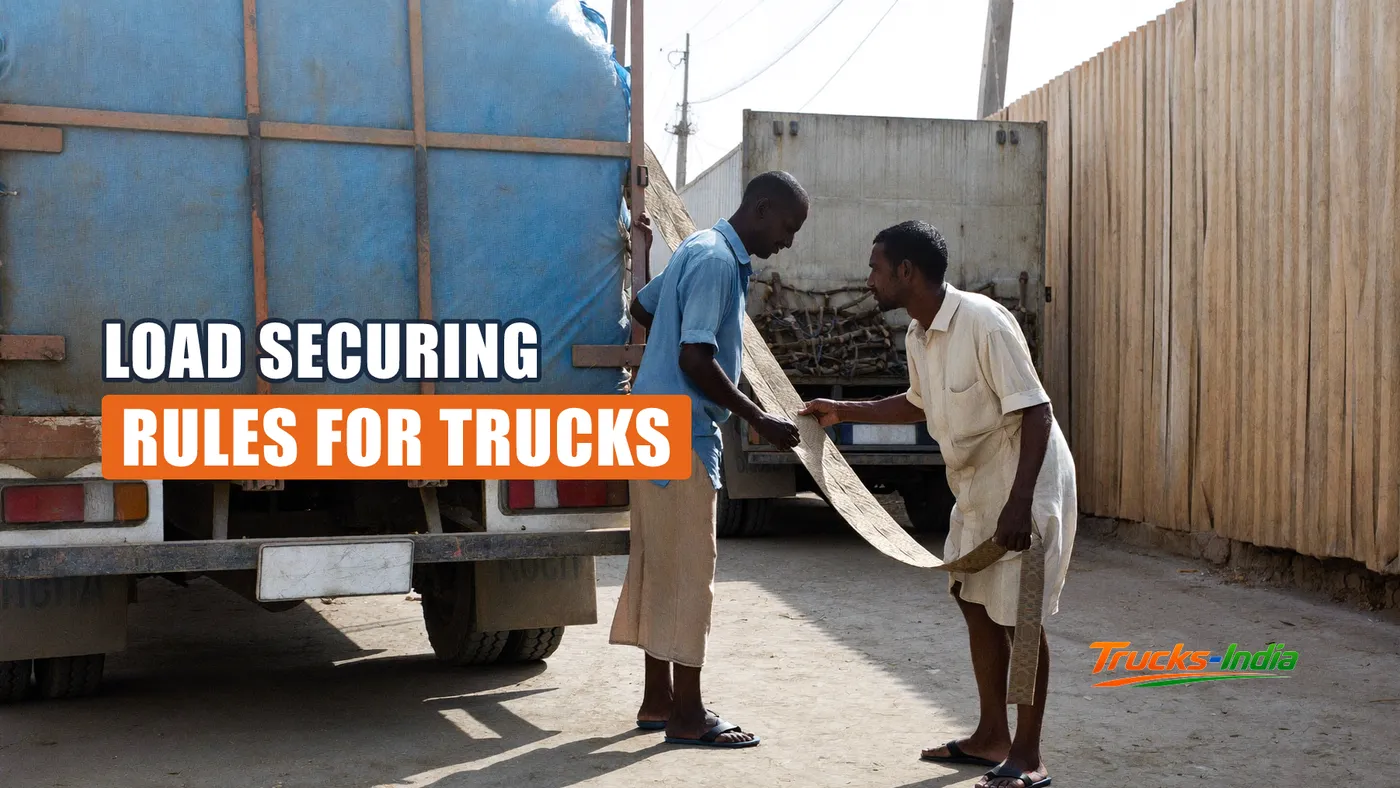 Two loaders pulling a webbing strap over the load on an open body truck in an Indian yard