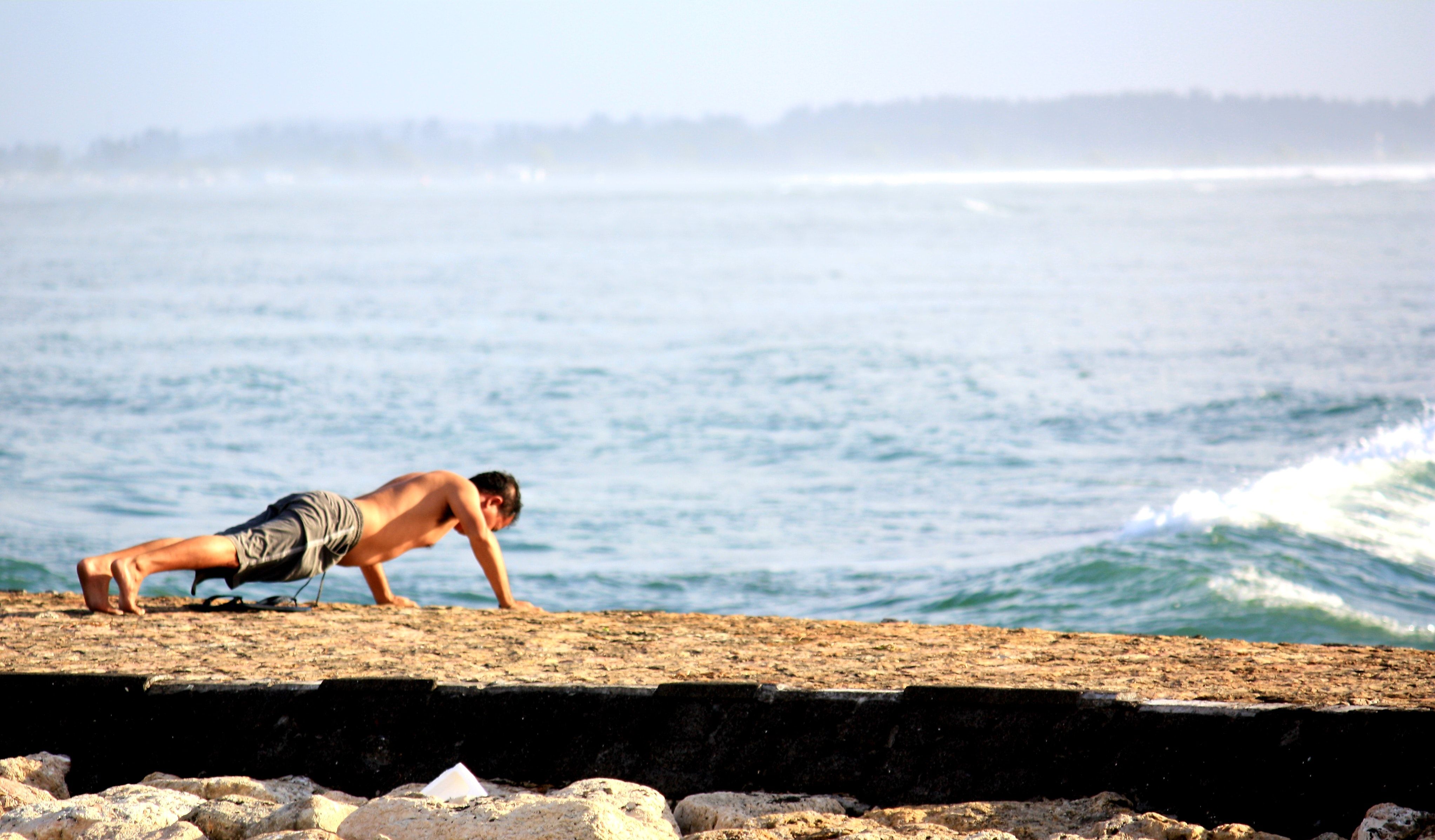 Male bodybuilder doing push-ups near the ocean