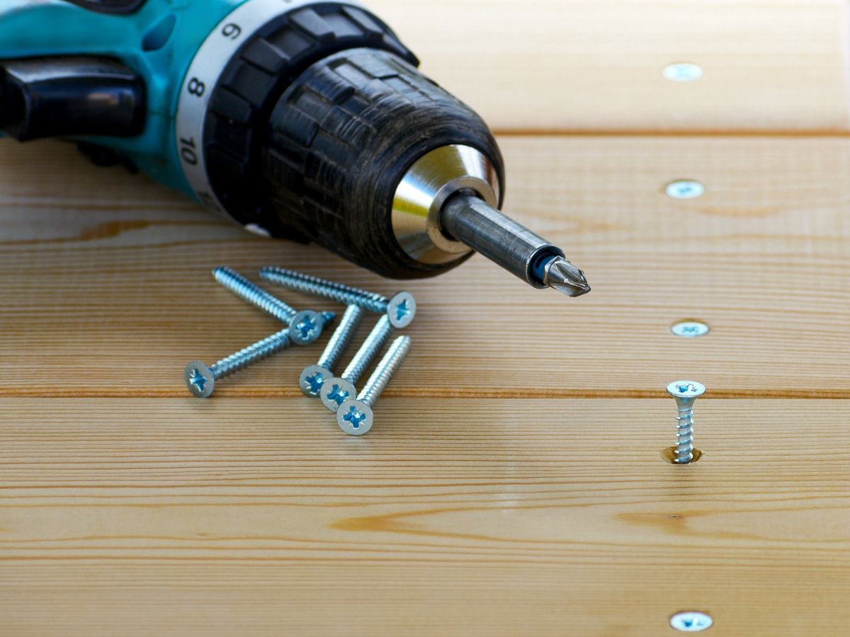 Cordless drill driving a screw into treated deck boards