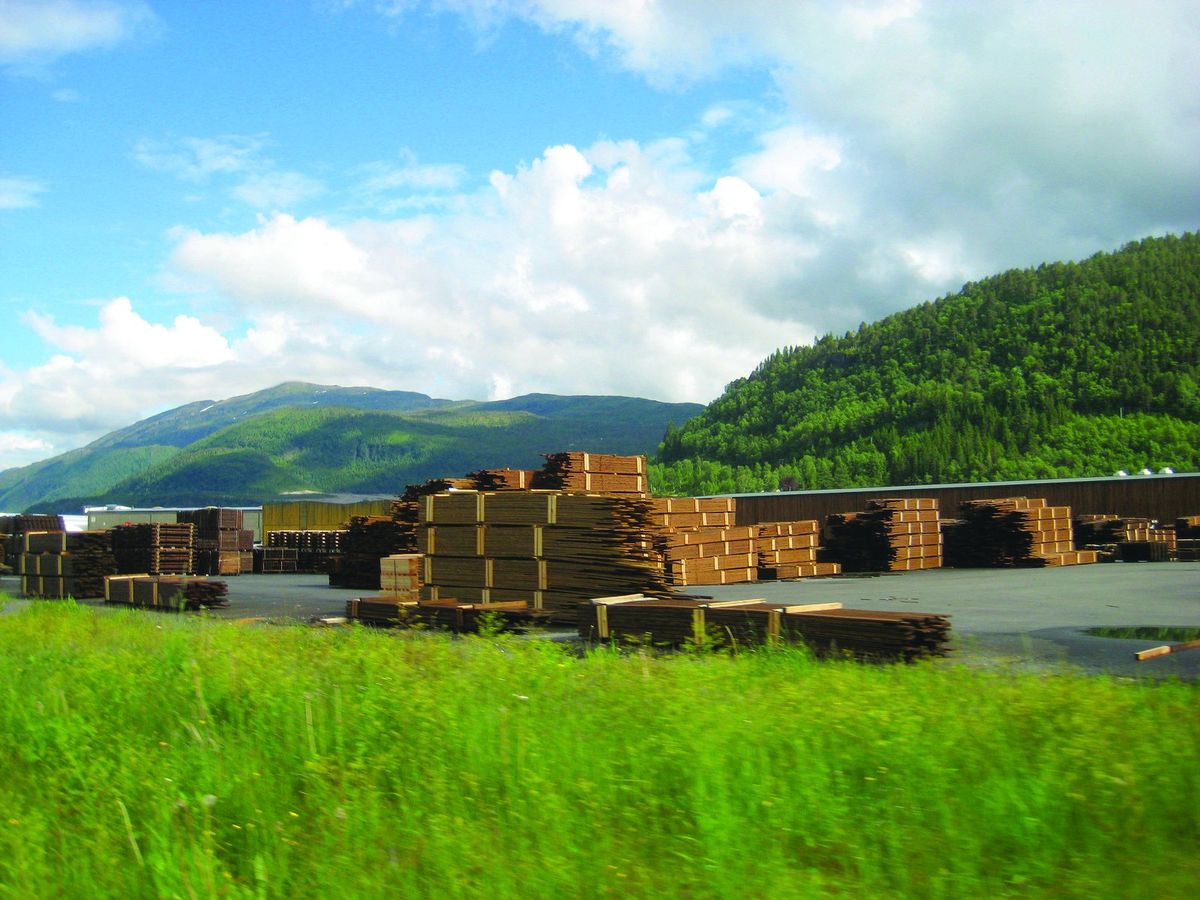 Stacks of treated lumber in a yard below green mountains