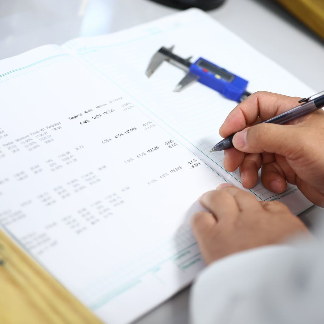 Hands recording measurements beside calipers and a wood sample