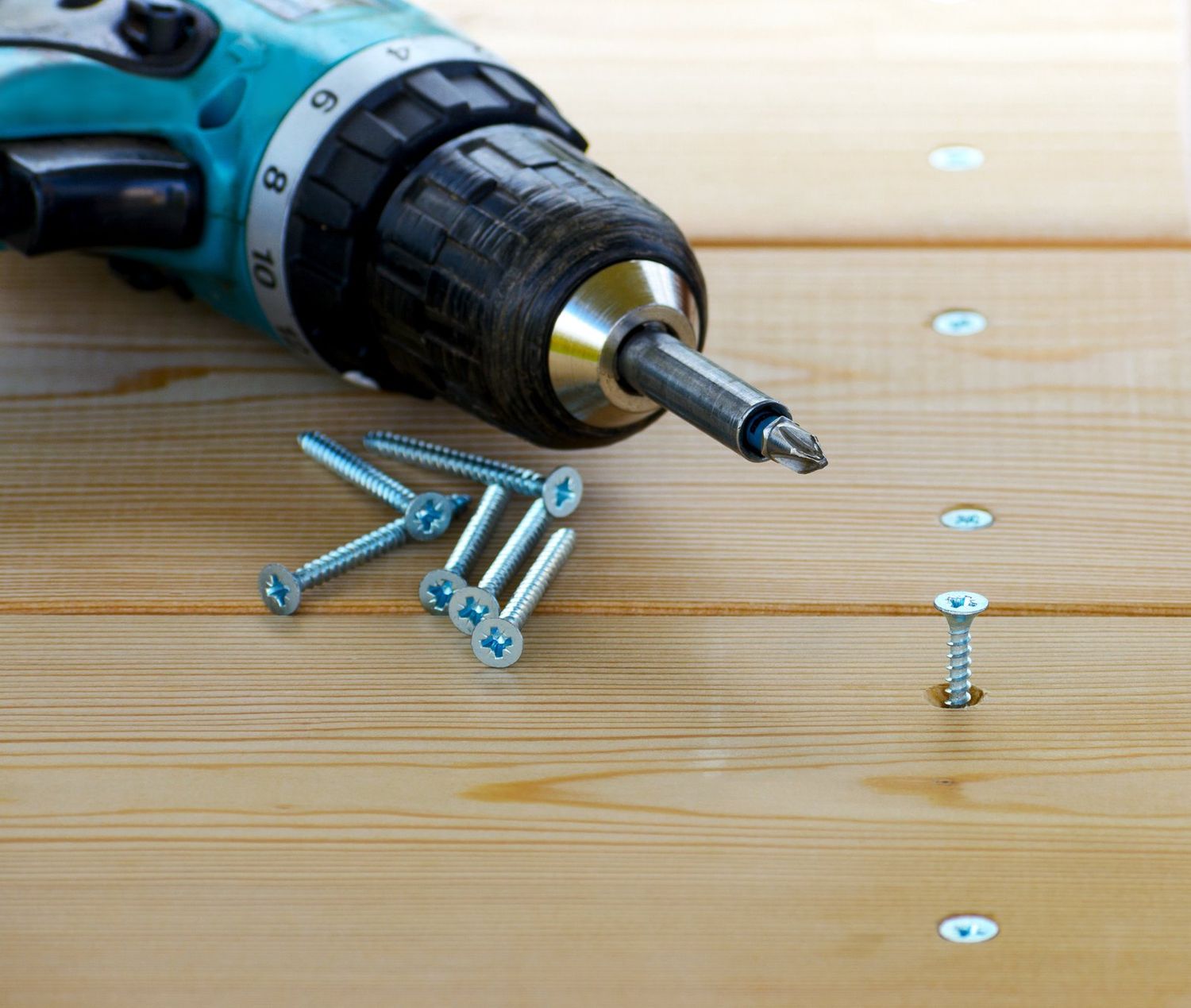 Cordless drill driving a screw into treated deck boards