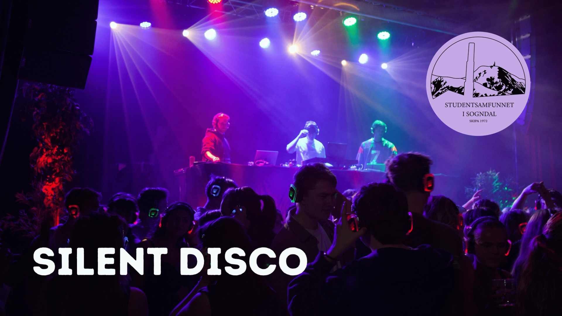 Fargerikt lys setter stemningen på en silent disco der en stor folkemengde danser med hodetelefoner foran en scene med tre DJ-er, og logoen til Studentsamfunnet i Sogndal vises øverst til høyre.