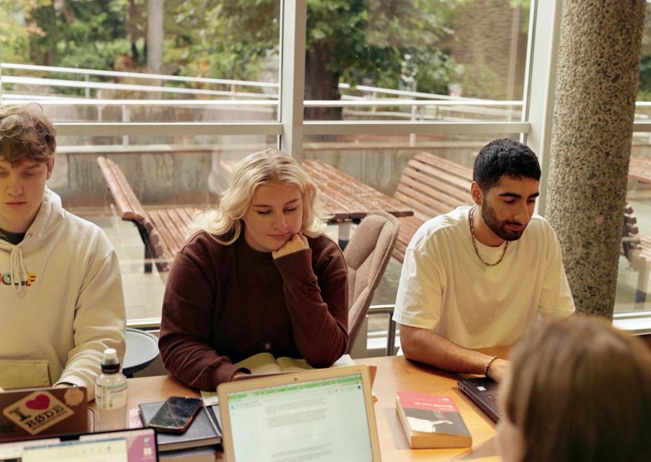 Three students sit together at a table working on laptops.