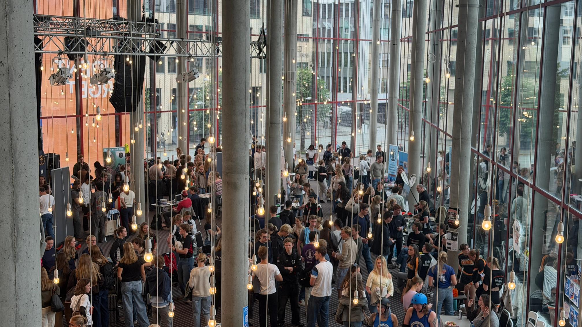 En stor gruppe studenter poserer foran en modernistisk bygning med et stort oransje banner med teksten «Studenttorget».