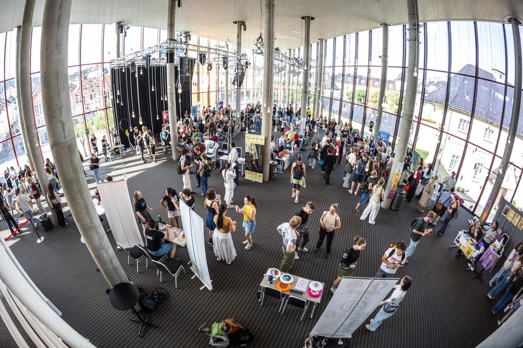 Oversiktsbilde av en lys og moderne messehall der mange studenter går rundt mellom ulike stands og prater med representanter for studentorganisasjoner.