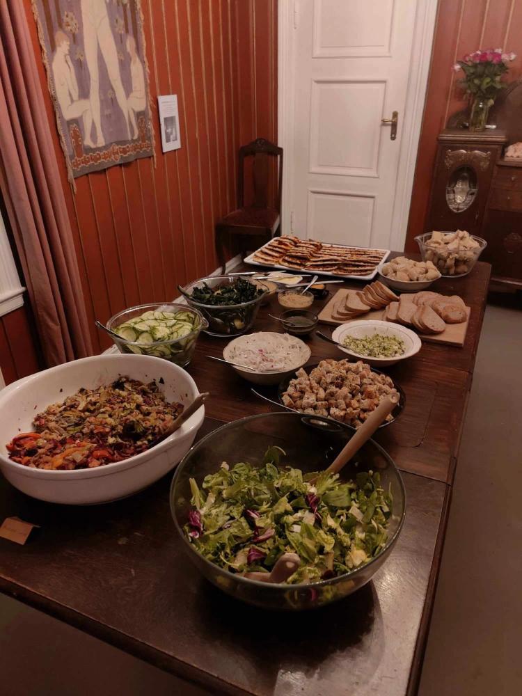 Et langbord er dekket med en variert buffé av salater, grønnsaksretter, brød, pålegg og andre småretter i et rom med røde trevegger.