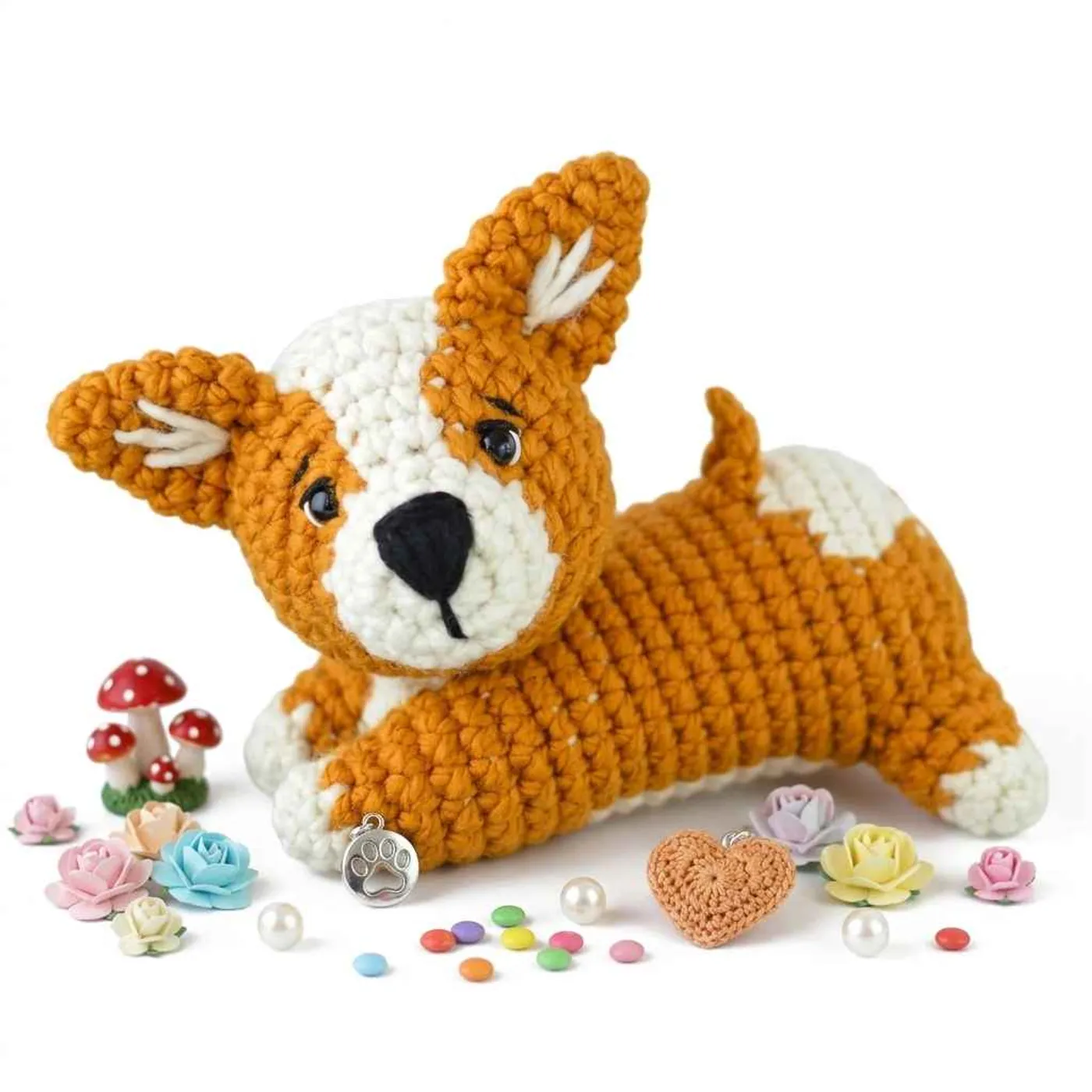 Orange and cream crochet corgi puppy lying down, with a cream blaze on the face, black safety eyes, an embroidered black nose, upright orange ears with cream lines inside, cream front paws and a short