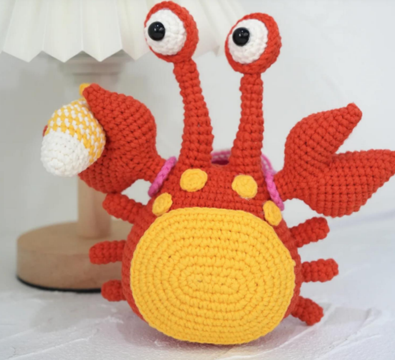 A cute handmade pink crochet crab with a shell bag and a tiny fish friend, part of a free amigurumi tutorial.
