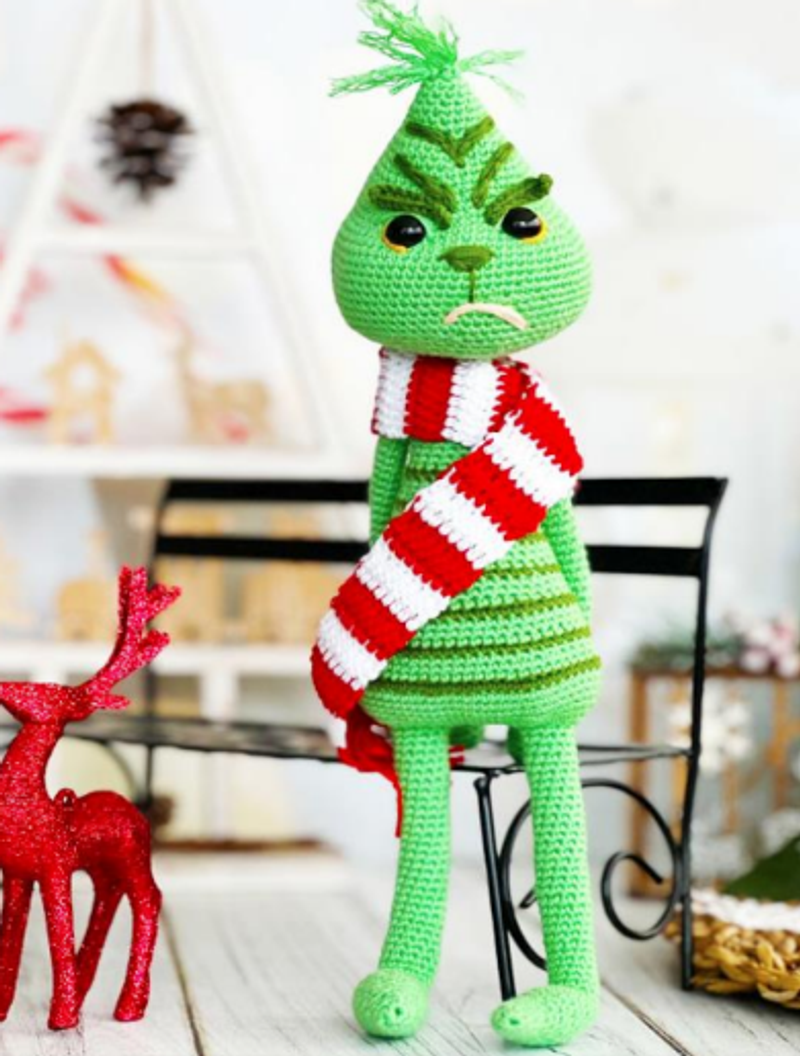 Tall, slender green crochet Grinch amigurumi doll with a grumpy face, poseable wire limbs, and a red and white striped scarf. Free pattern.