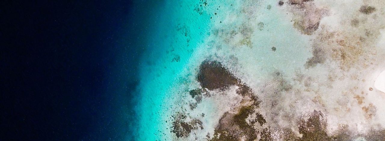 Vista aérea de un arrecife y aguas turquesa junto a mar profundo