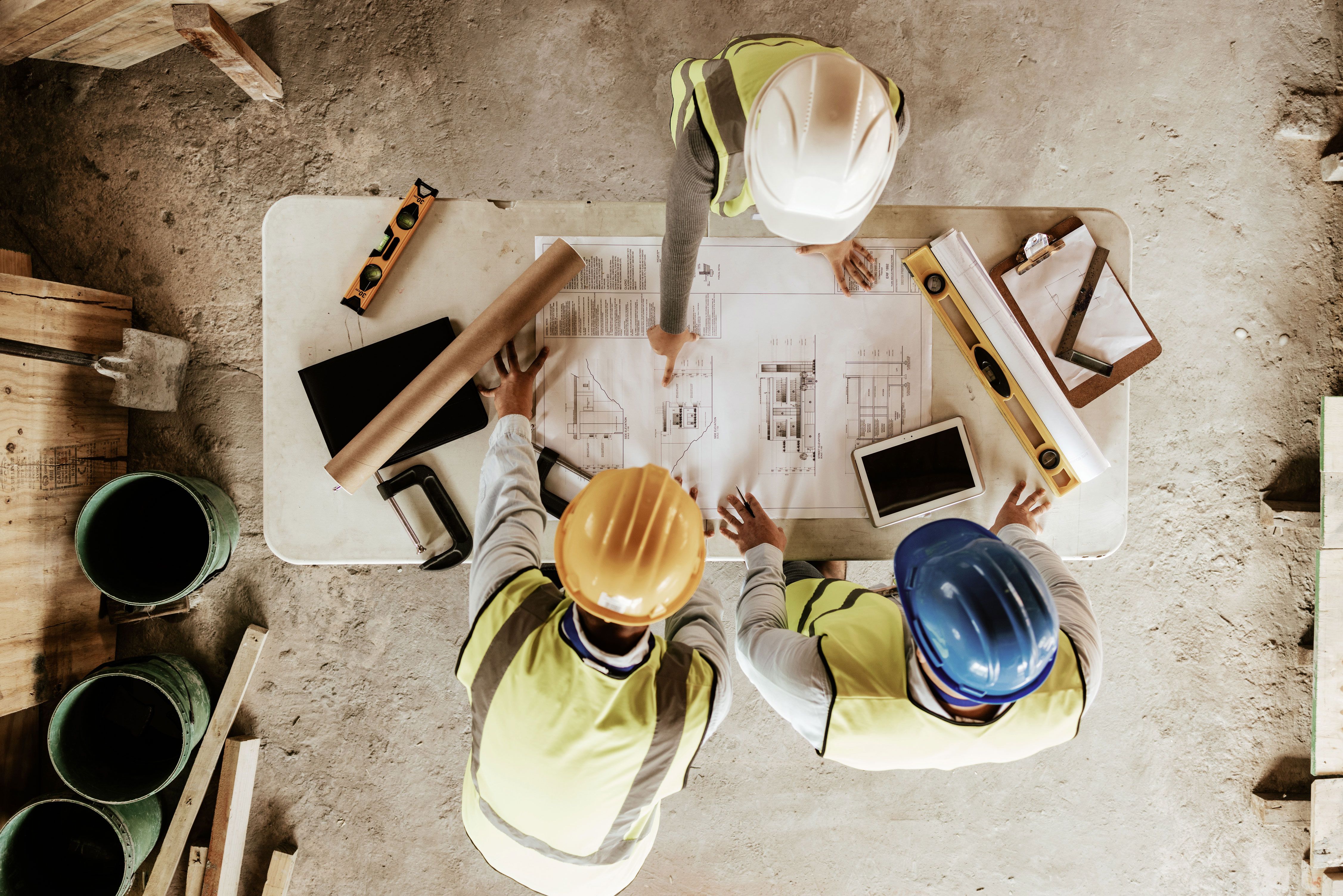 construction workers in hardhats looking at plans around table 