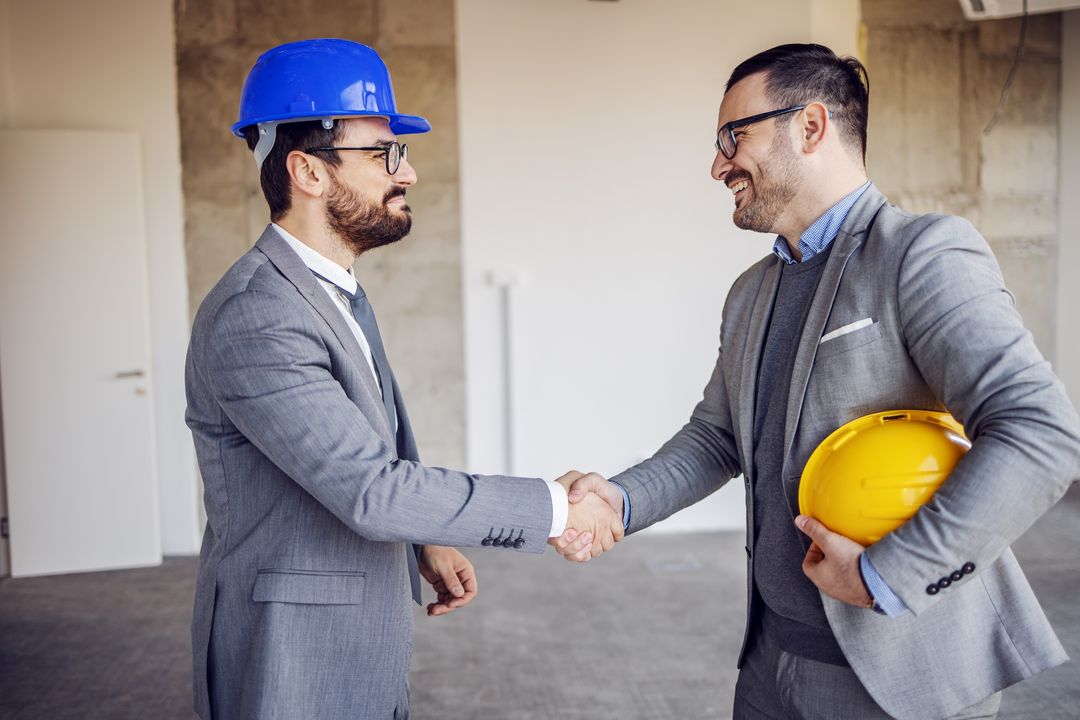 Two men shaking hand with construction helmets