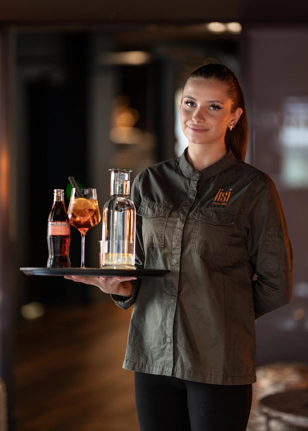 Eine Kellnerin bringt den Apéro auf dem Serviertablett: Aperol Spritz, Coca Cola und Wasser