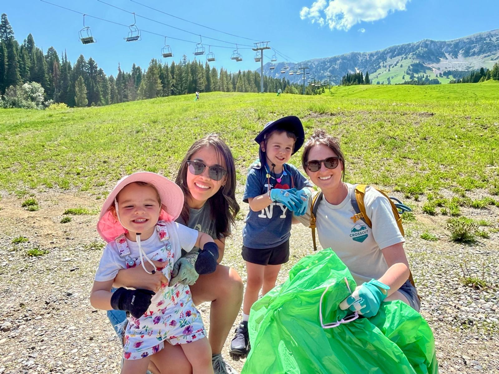 Volunteers collecting trash on a sunny summer day at Bridger Bowl with ski lifts and mountains in the background