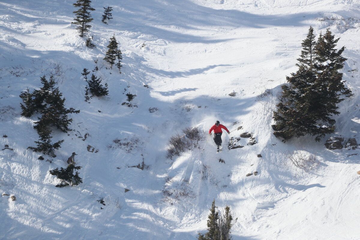 Skier in a red jacket descending a snowy chute.