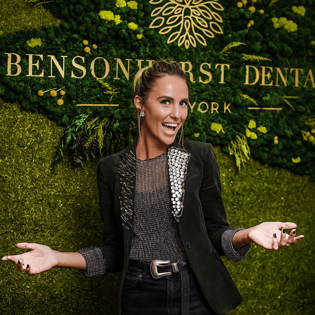 Smiling patient in front of the Bensonhurst Dental moss wall logo