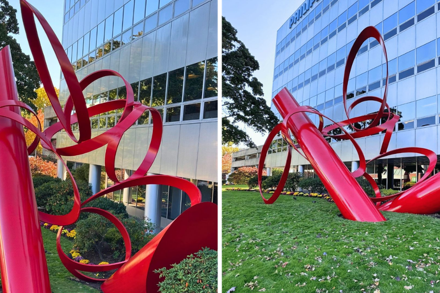 Two views of a glossy red looping steel sculpture on a lawn in front of a glass-and-panel office building with landscaped shrubs.