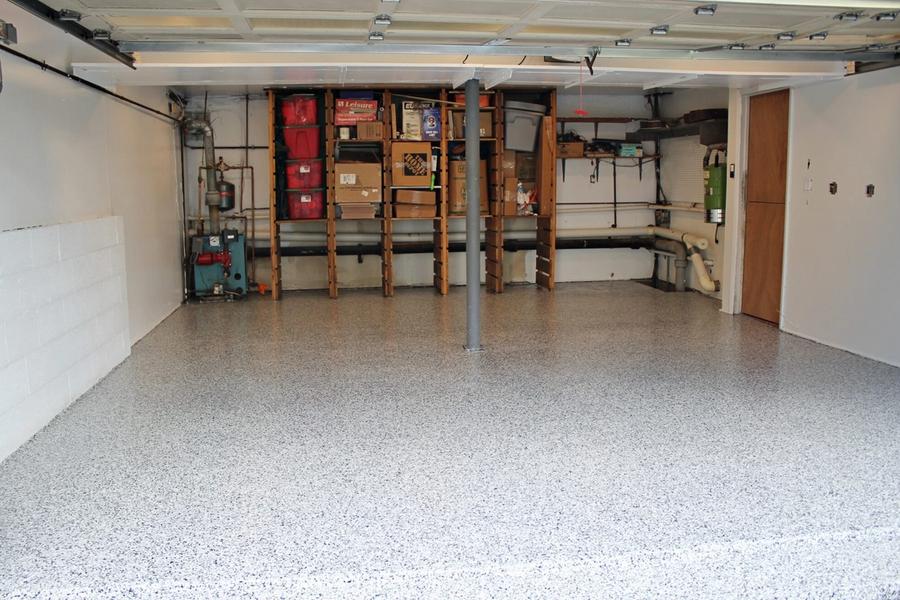 Two-car garage interior with a gray-and-white speckled epoxy floor coating, wooden storage shelving holding bins and boxes along the back wall, and white walls and ceiling.