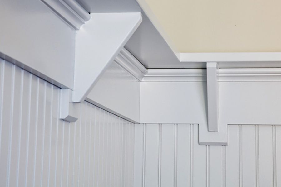 White painted beadboard wainscoting with a molded shelf rail and decorative brackets beneath crown molding and a pale yellow ceiling.