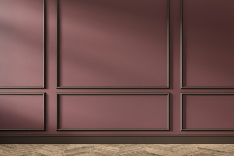 Interior wall painted muted mauve with dark brown picture-frame molding and baseboard trim above a herringbone wood floor.